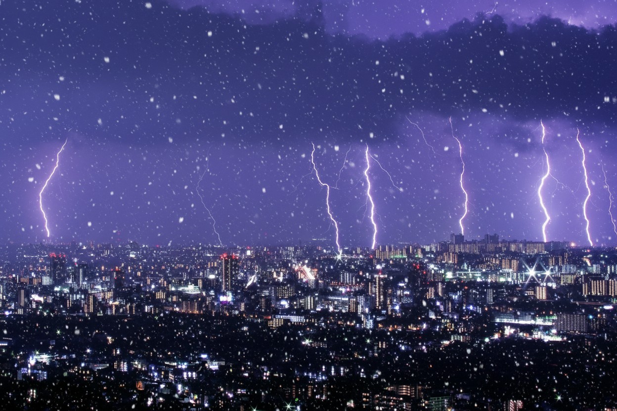 紫色の夜空に落ちる激しい雷と都市夜景の幻想的な写真。雪が舞う冬の嵐を捉えた高品質な風景画像。